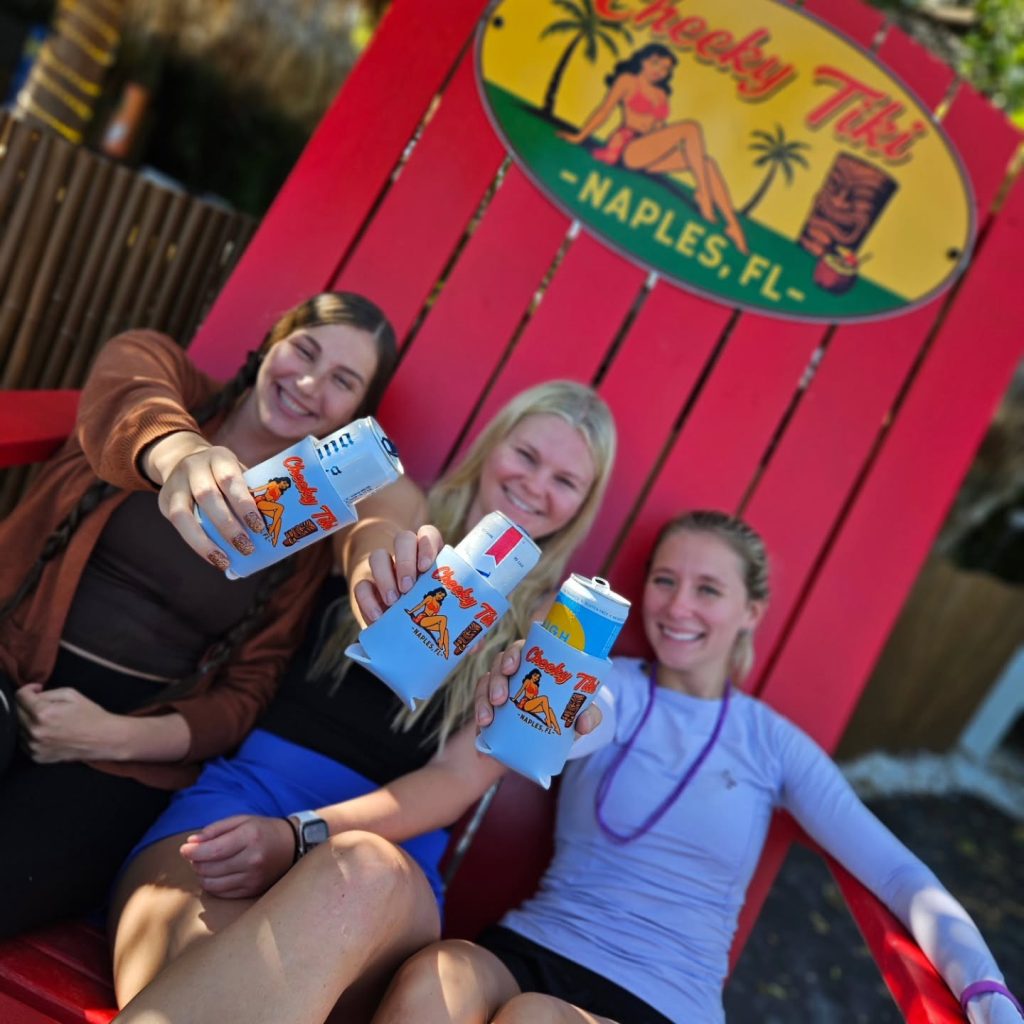 Three friends squeezed into the giant red Cheeky Tiki chair, raising koozies