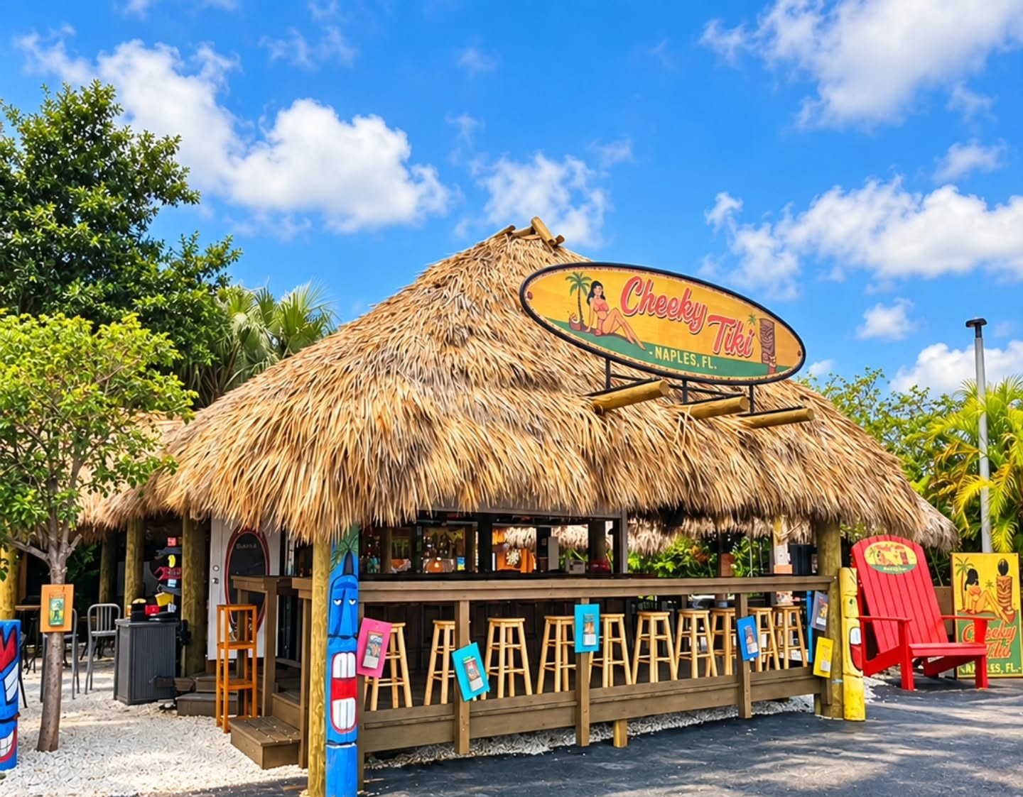 The Cheeky Tiki bar hut on a sunny day with its surfboard sign and red chairs